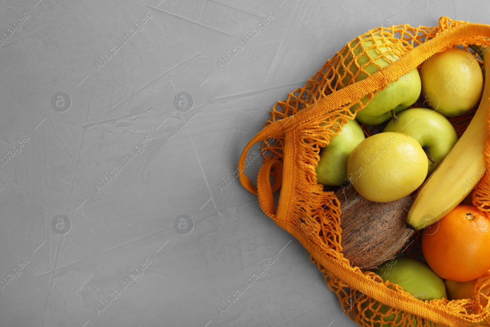 Photo of Net bag with fruits on light grey table, top view. Space for text