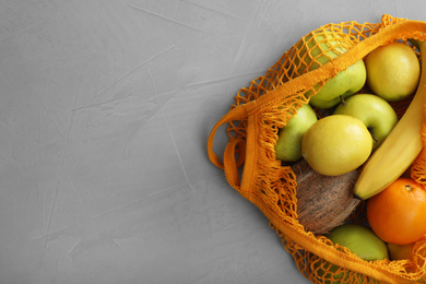 Net bag with fruits on light grey table, top view. Space for text