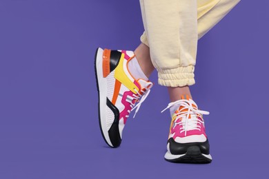 Woman wearing pair of new stylish sneakers on purple background, closeup