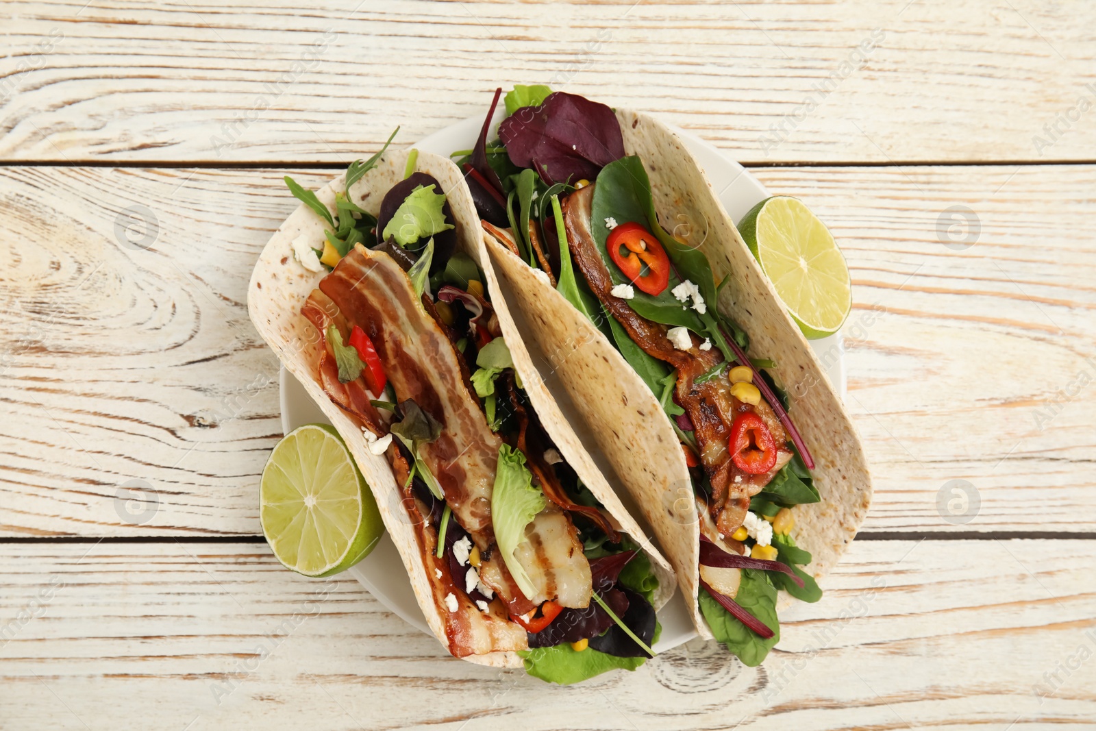 Photo of Delicious tacos with fried bacon and lime on white wooden table, flat lay