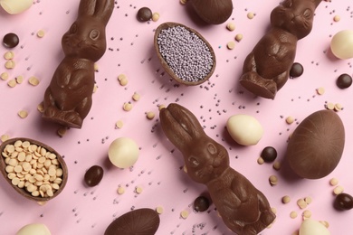 Flat lay composition with chocolate Easter bunnies, eggs and candies on pink background