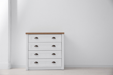 Photo of Modern white chest of drawers near light wall in room, space for text. Interior design