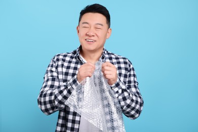 Photo of Happy asian man with bubble wrap on light blue background