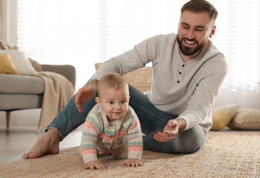 Photo of Happy young father helping his cute baby to crawl on floor at home