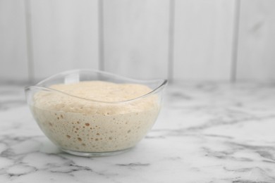 Photo of Leaven in glass bowl on white marble table, space for text
