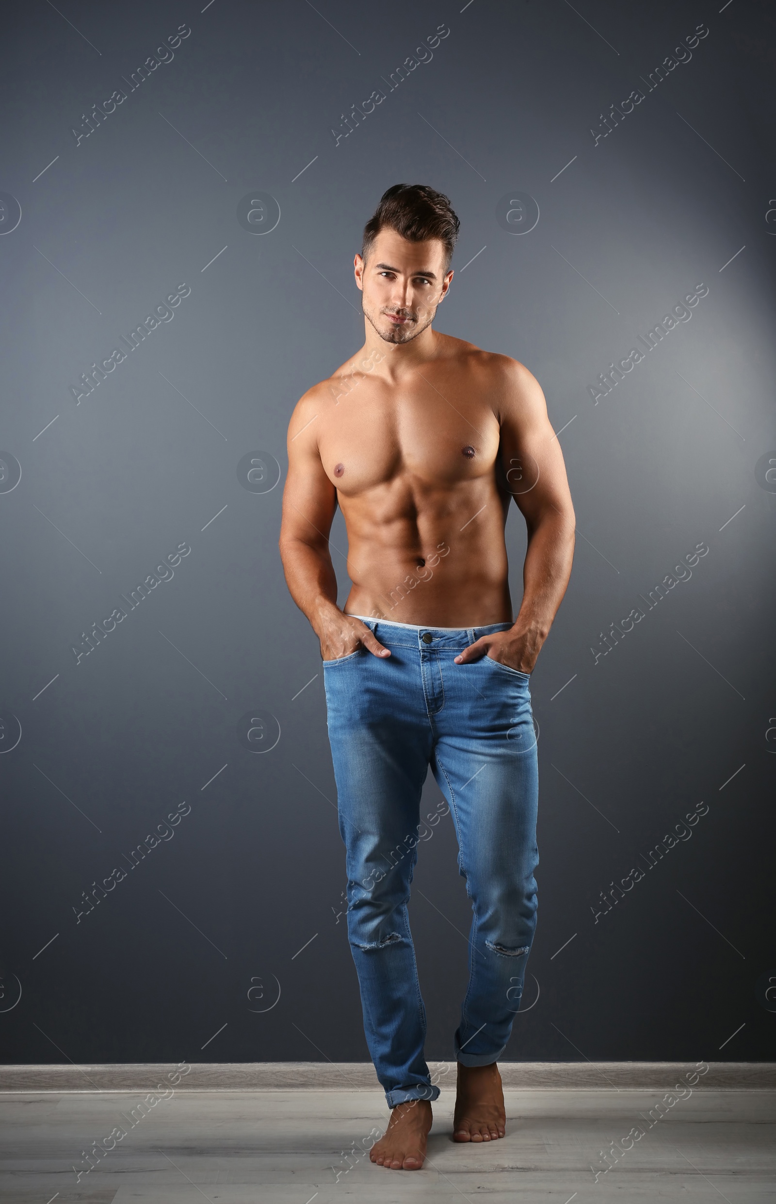 Photo of Shirtless young man in stylish jeans near grey wall