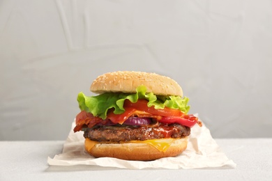 Photo of Tasty burger with bacon on table against grey background