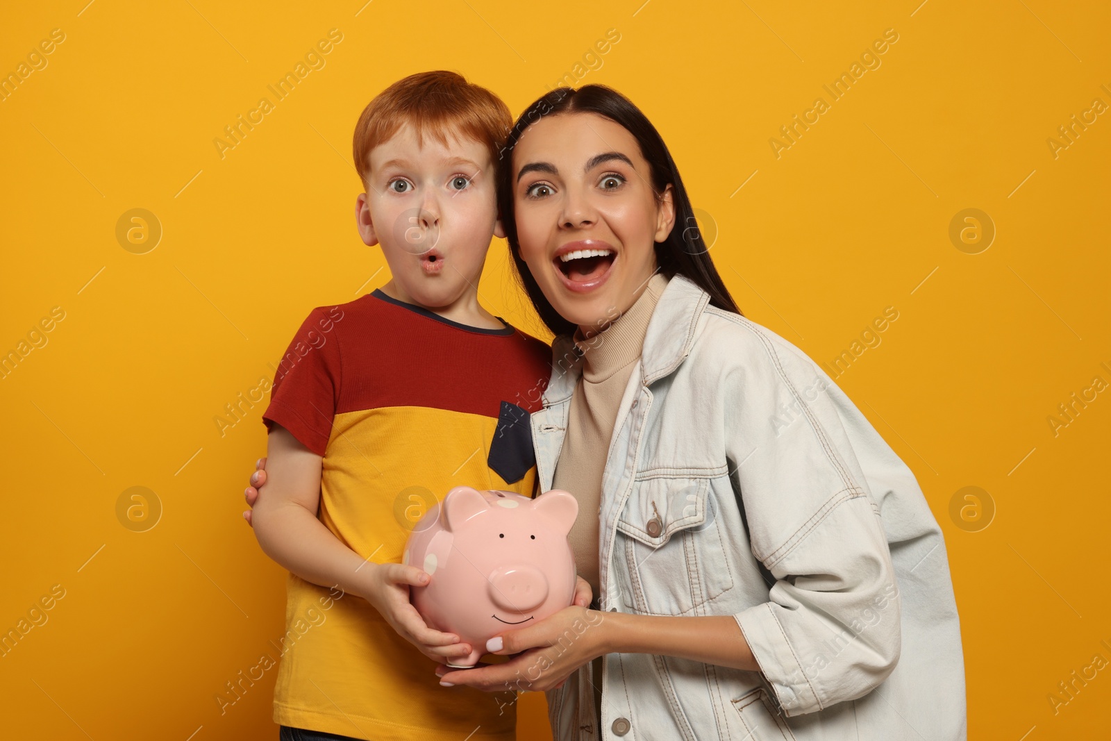 Photo of Mother and her son with ceramic piggy bank on orange background