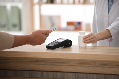 Photo of Customer using terminal for contactless payment with smartphone in pharmacy, closeup