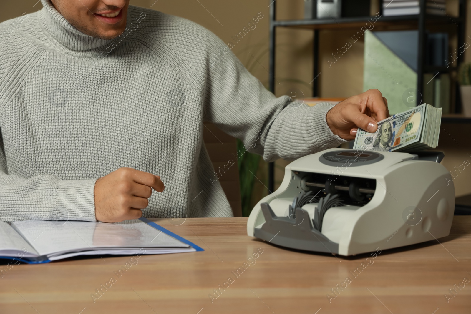 Photo of Man putting money into banknote counter at wooden table indoors, closeup