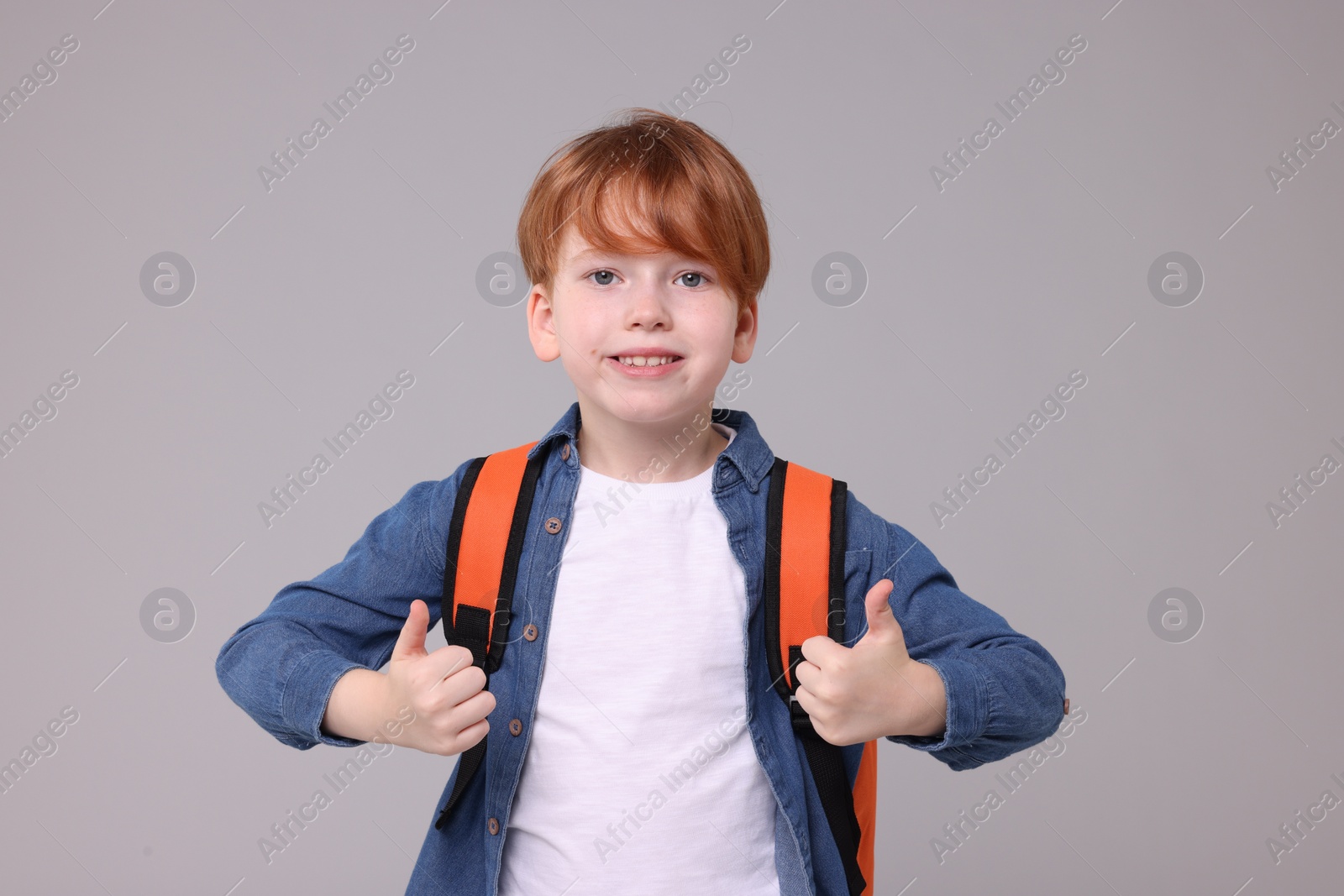 Photo of Happy schoolboy showing thumbs up on grey background