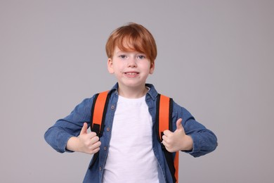 Photo of Happy schoolboy showing thumbs up on grey background