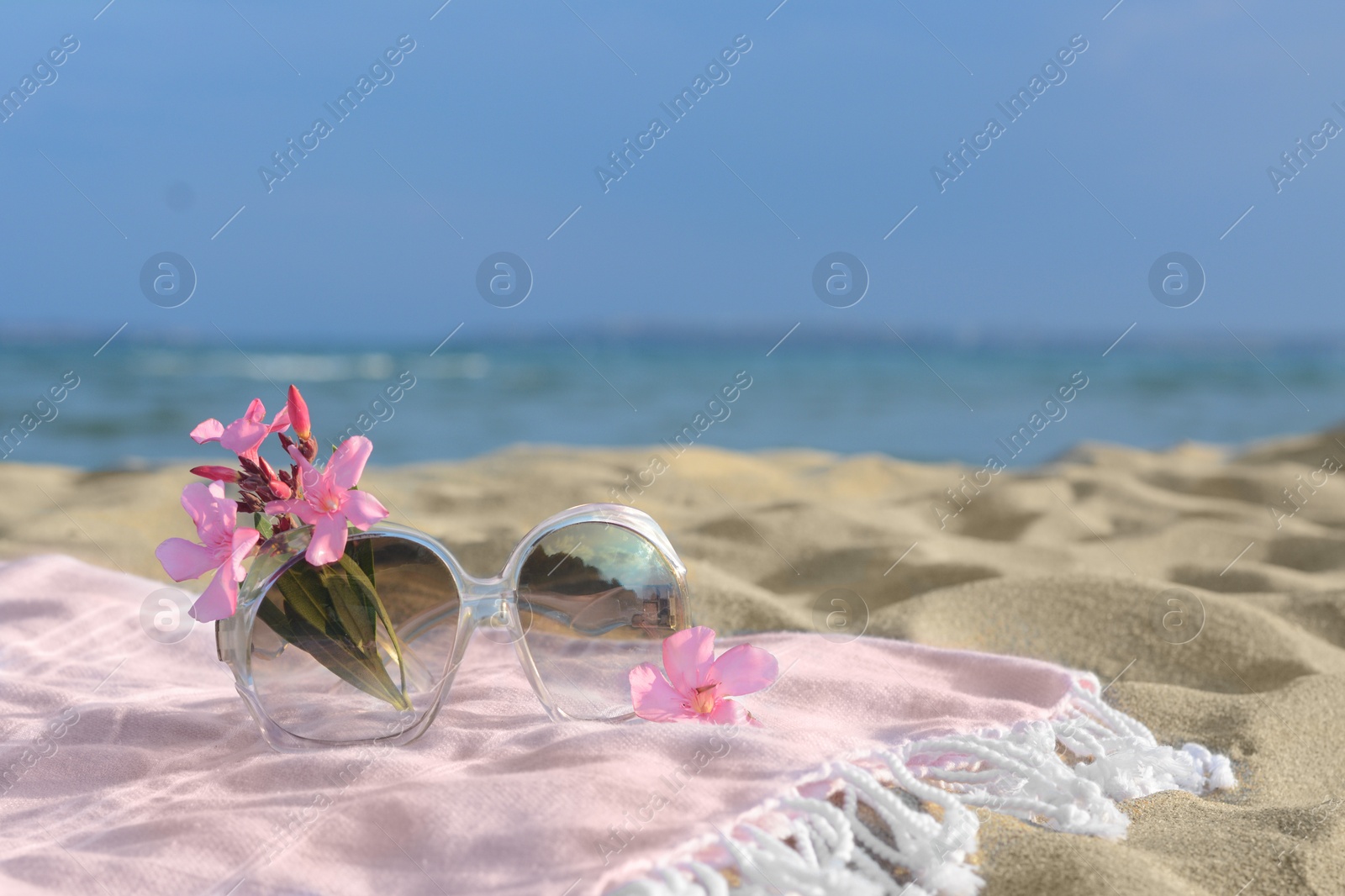 Photo of Beautiful sunglasses with tropical flower on blanket near sea. Space for text