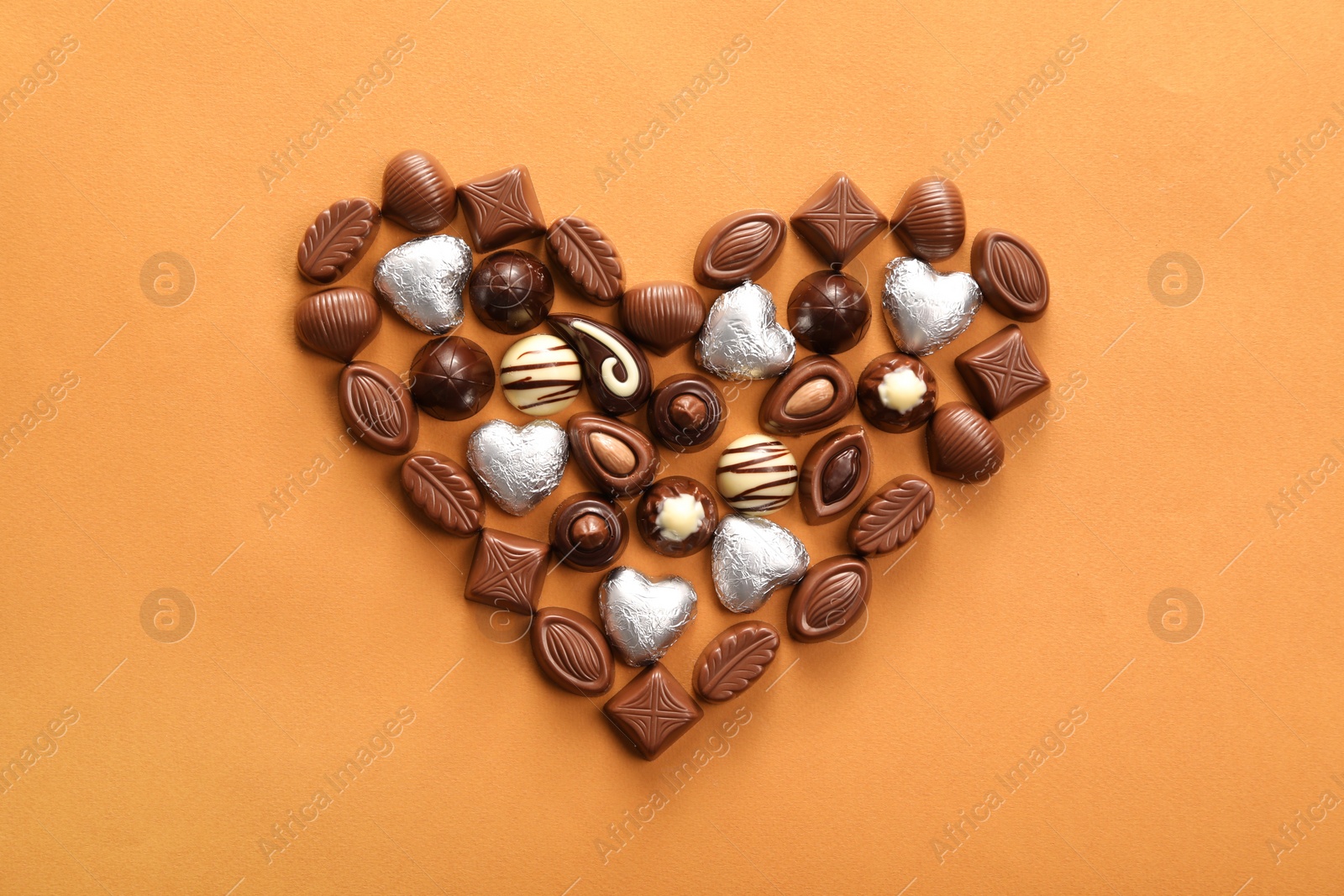 Photo of Heart made with delicious chocolate candies on brown background, top view