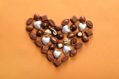 Heart made with delicious chocolate candies on brown background, top view