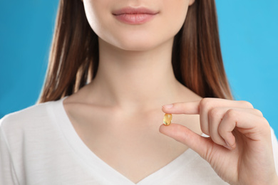 Photo of Young woman with vitamin pill on blue background, closeup