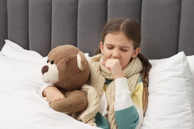 Photo of Sick girl with teddy bear coughing on bed at home