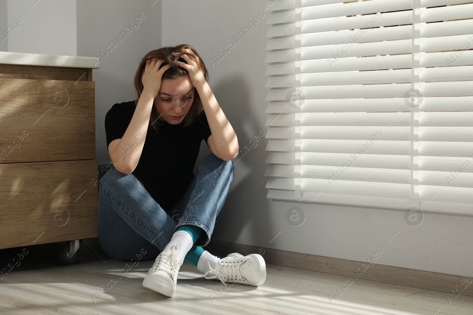 Photo of Sad young woman sitting on floor indoors, space for text