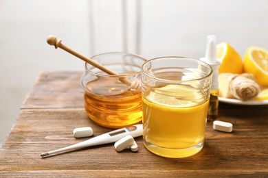 Photo of Glass with hot tea, honey and pills for cold on wooden table