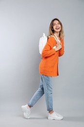 Happy woman with backpack on light grey background