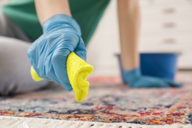 Photo of Woman in rubber gloves cleaning carpet with rag indoors, closeup. Space for text