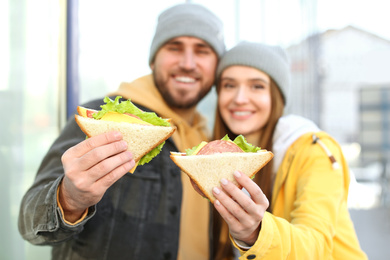 Happy young couple with sandwiches on city street