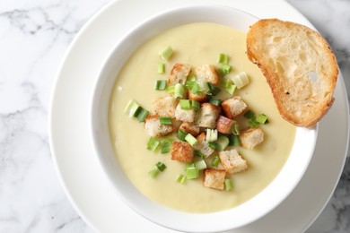 Photo of Tasty potato soup with croutons and green onion in bowl on white marble table, top view