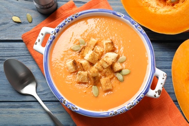 Photo of Tasty creamy pumpkin soup with croutons and seeds in bowl on blue wooden table, flat lay