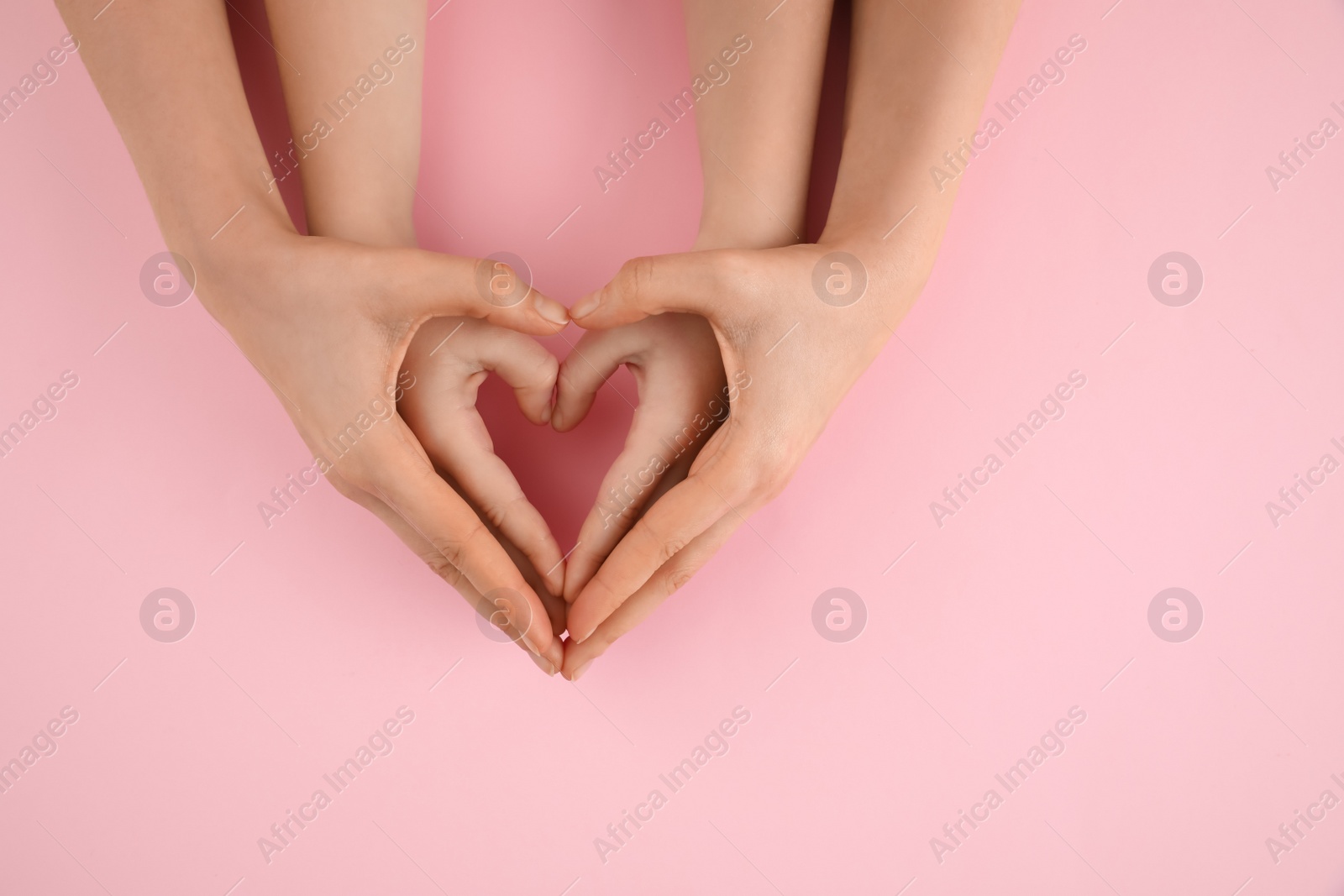 Photo of Mother holding hands with her child on pink background, top view