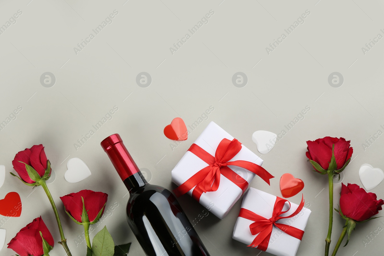 Photo of Beautiful gift boxes, roses and wine on grey background, flat lay with space for text. Valentine's day celebration