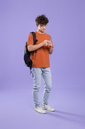 Photo of Cute teenage boy using smartphone on violet background