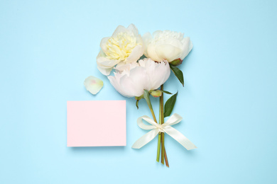 Beautiful bouquet of fresh peonies and blank card on light blue background, flat lay. Space for text