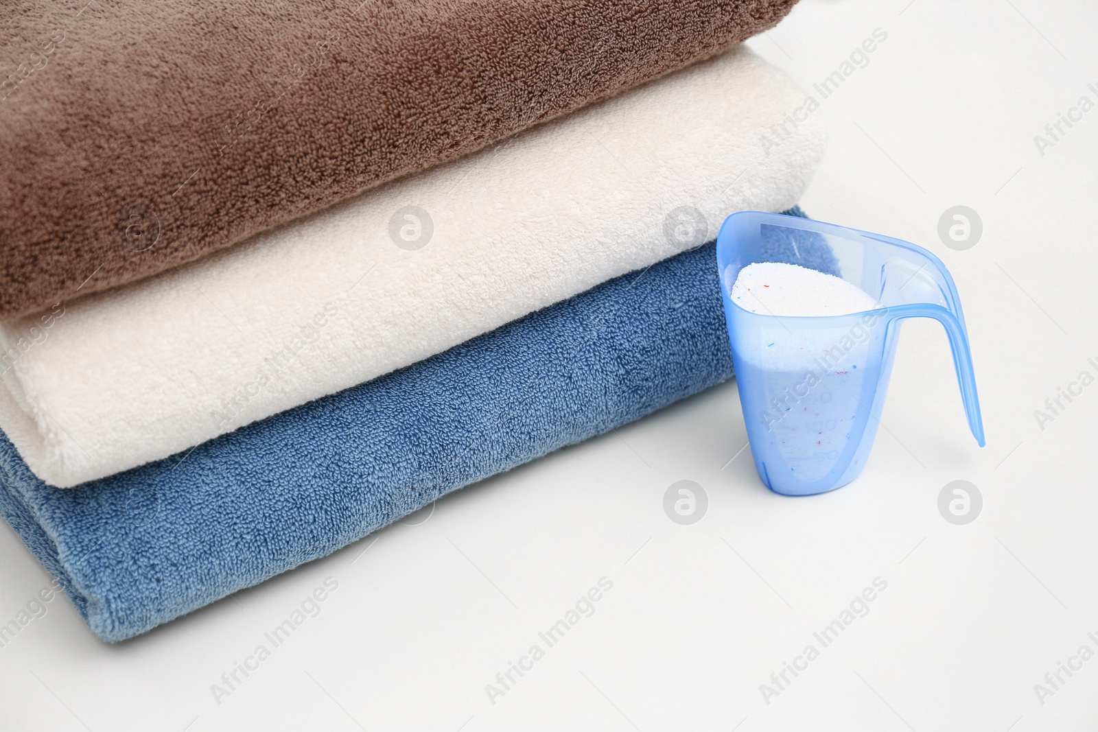 Photo of Clean towels and measuring cup of washing powder on table