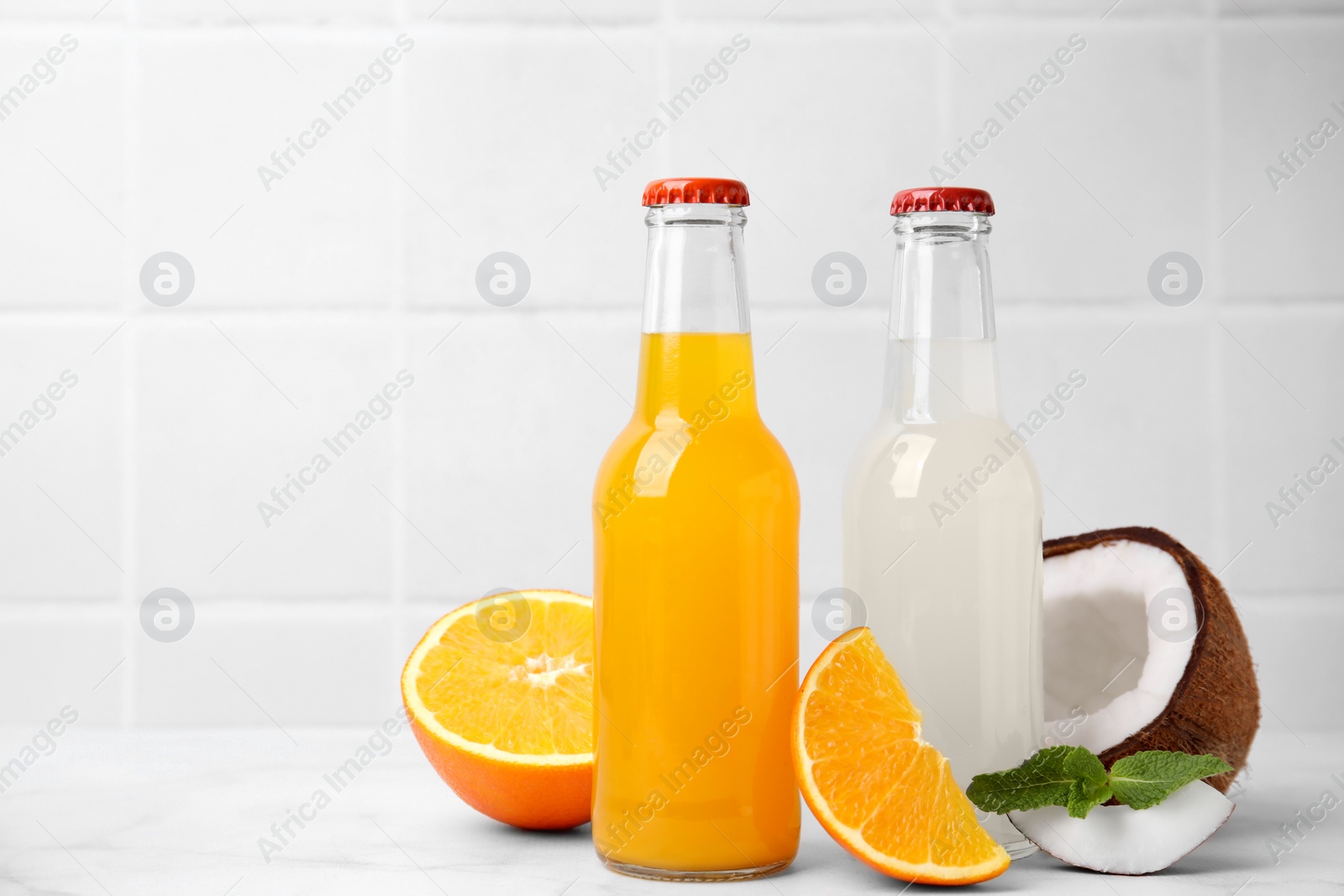 Photo of Delicious kombucha in glass bottles, orange, coconut and mint on white marble table, space for text