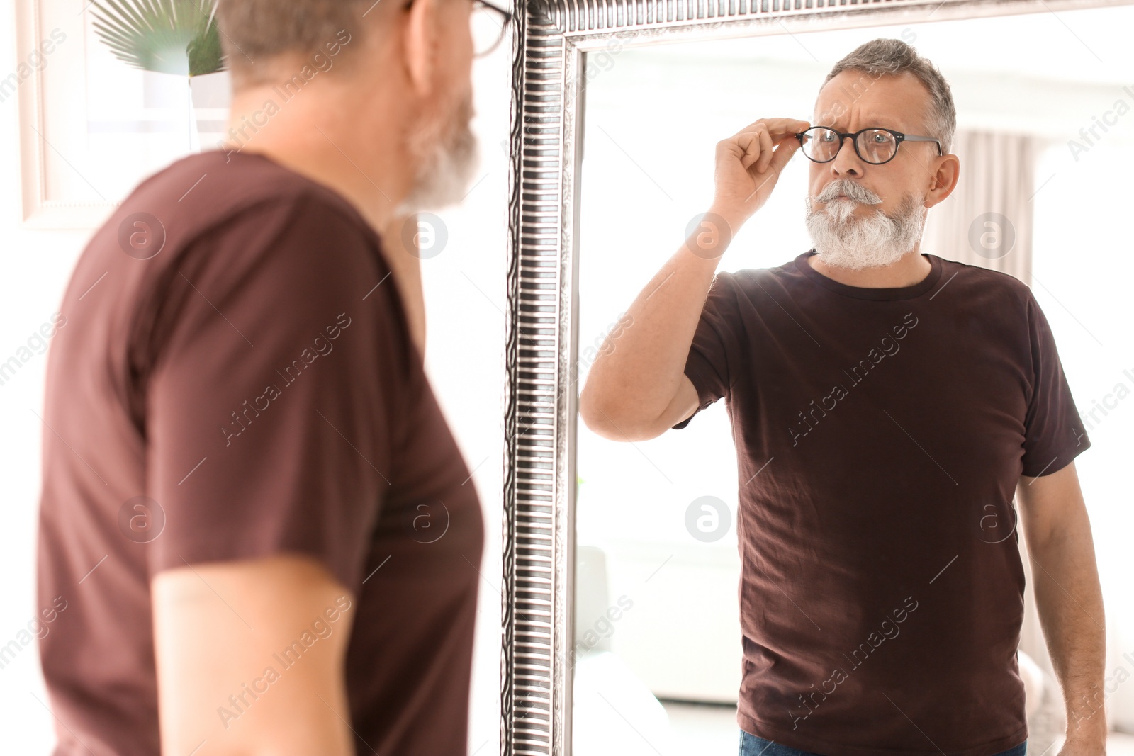 Photo of Mature man looking in mirror at home