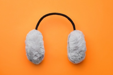 Stylish winter earmuffs on orange background, top view