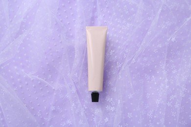 Photo of Tube of hand cream and fabric on violet background, top view