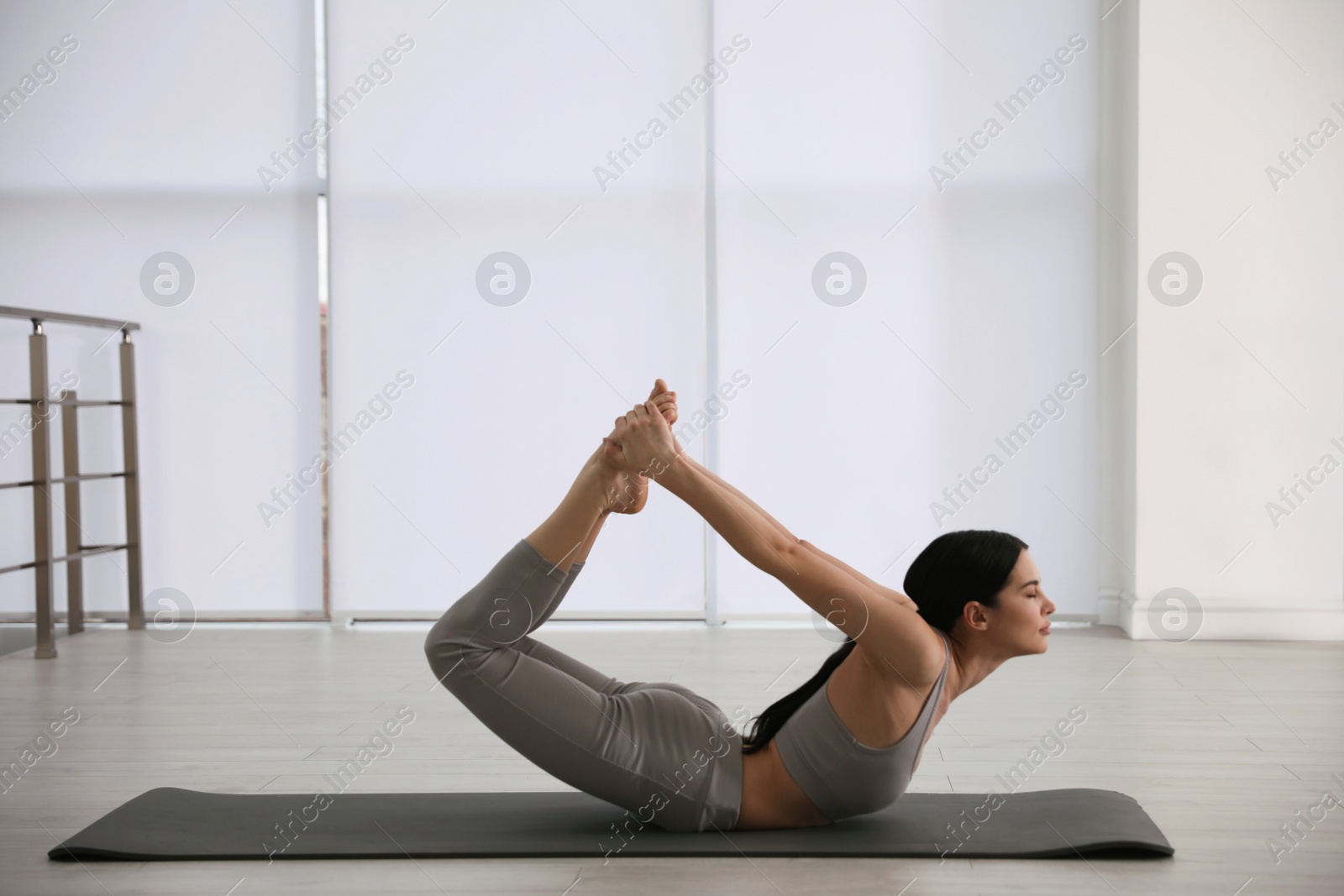 Photo of Young woman practicing bow asana in yoga studio. Dhanurasana pose