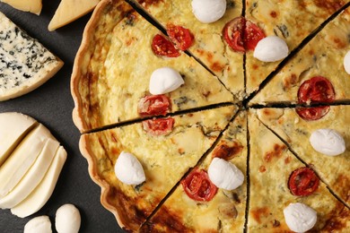 Photo of Delicious homemade cheese quiche and ingredients on black table, flat lay