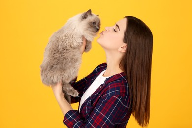 Photo of Woman kissing her cute cat on orange background