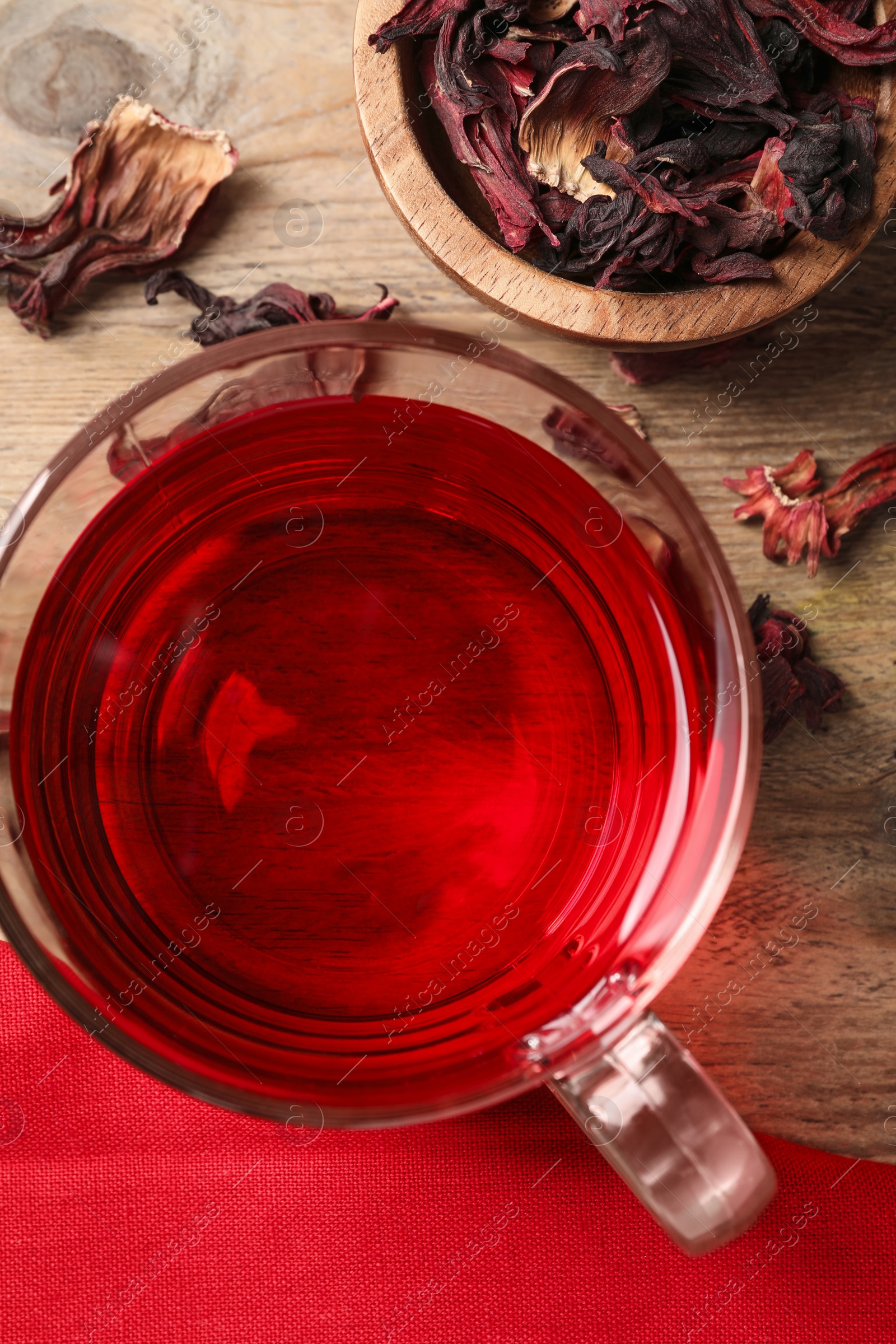 Photo of Cup of fresh hibiscus tea and dry flower leaves on wooden table, flat lay