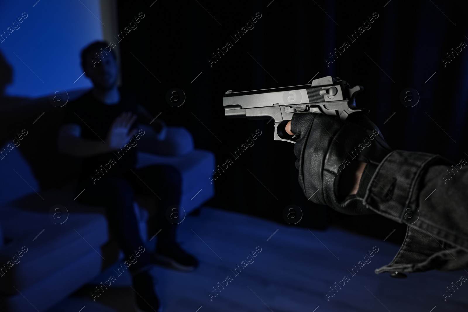 Photo of Man aiming his victim with gun in dark room, closeup. Dangerous criminal