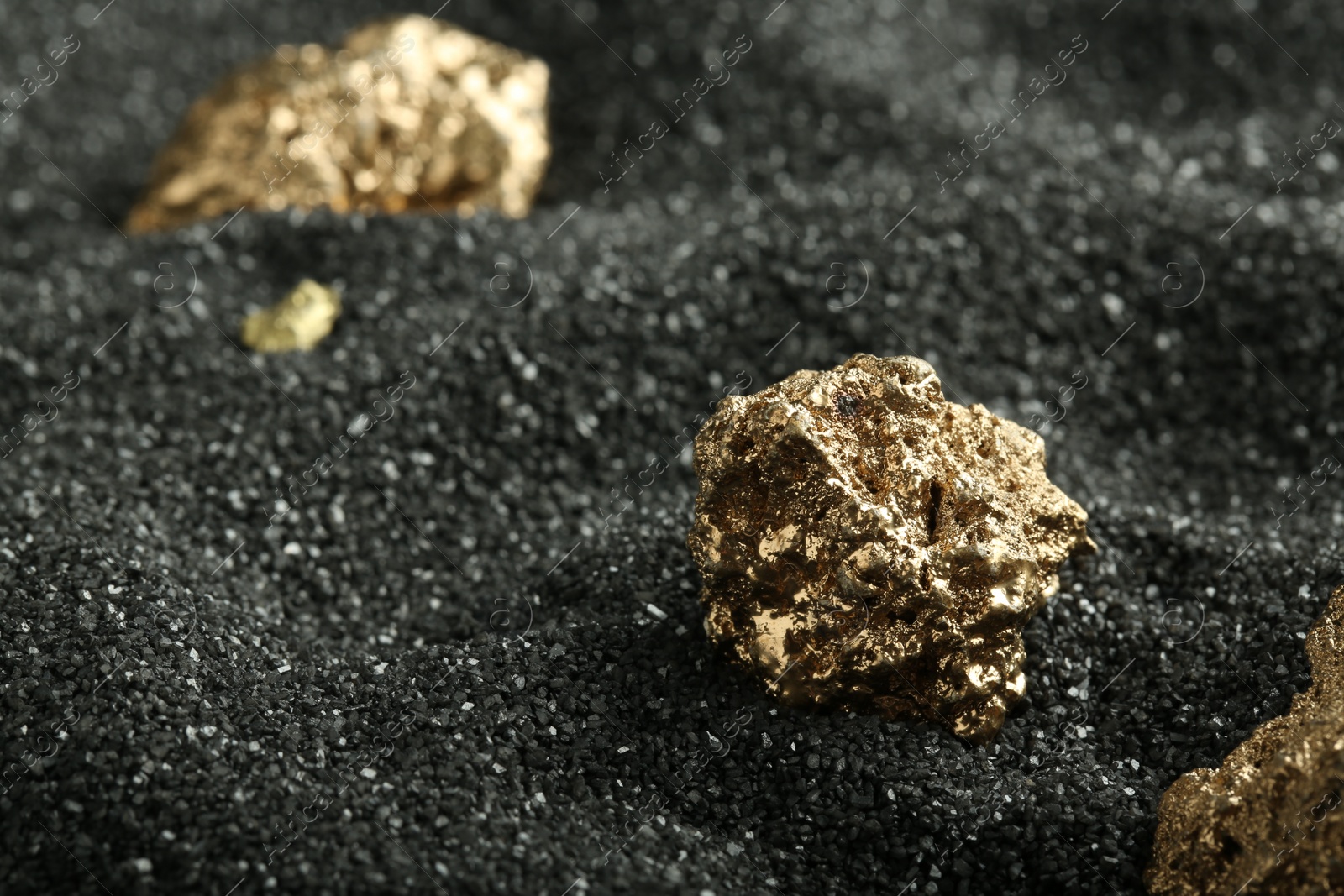 Photo of Shiny gold nuggets on black sand, closeup. Space for text