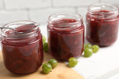 Photo of Jars of delicious gooseberry jam and fresh berries on white table, closeup