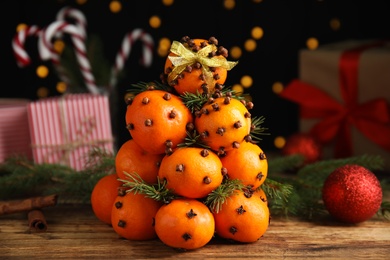 Photo of Pomander balls made of tangerines with cloves and fir branches on wooden table