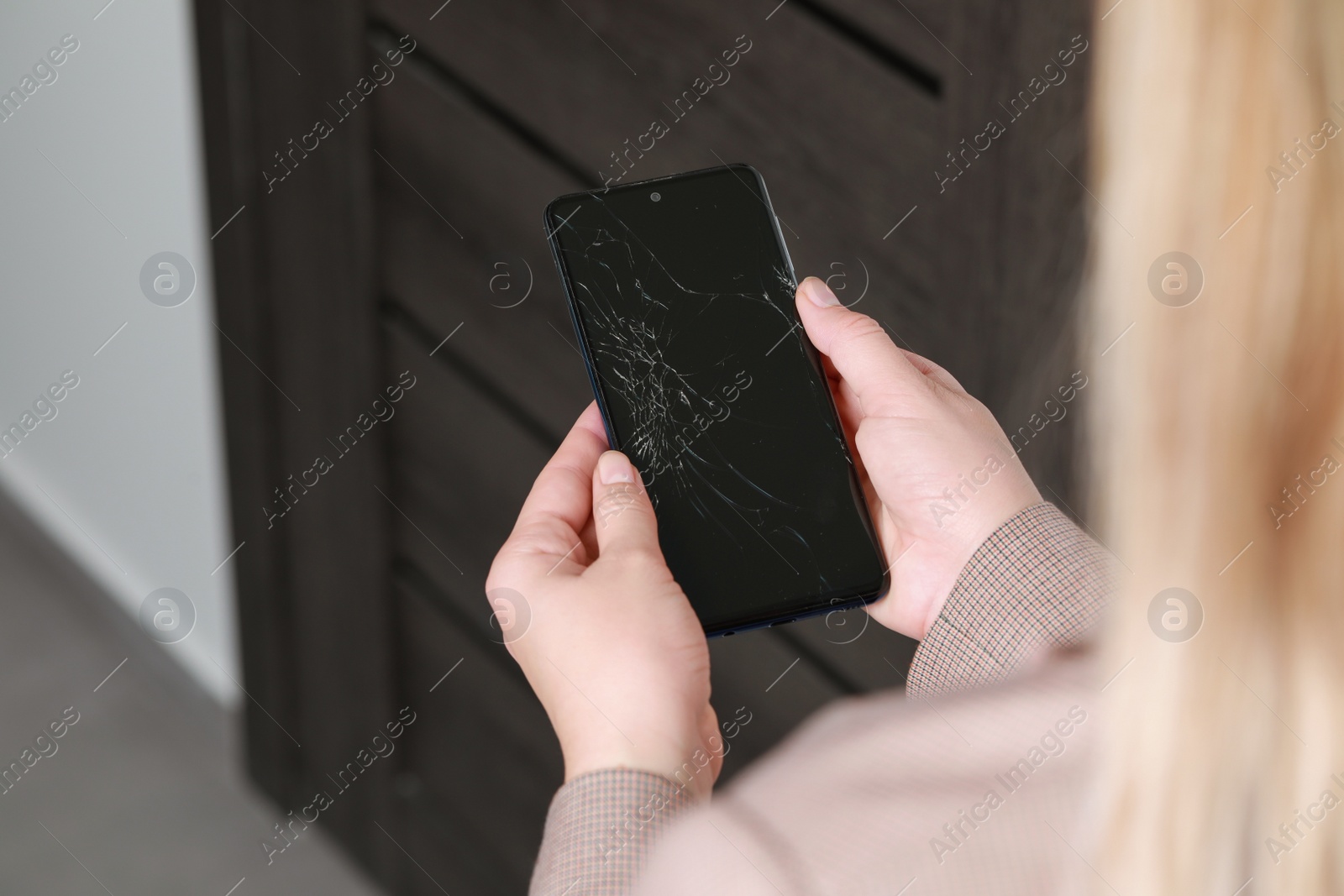 Photo of Woman holding damaged smartphone near door, closeup. Device repairing