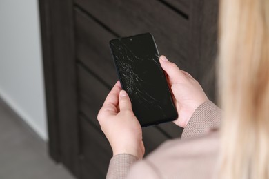 Photo of Woman holding damaged smartphone near door, closeup. Device repairing