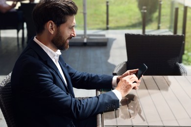 Photo of Handsome bearded man with smartphone at table in cafe