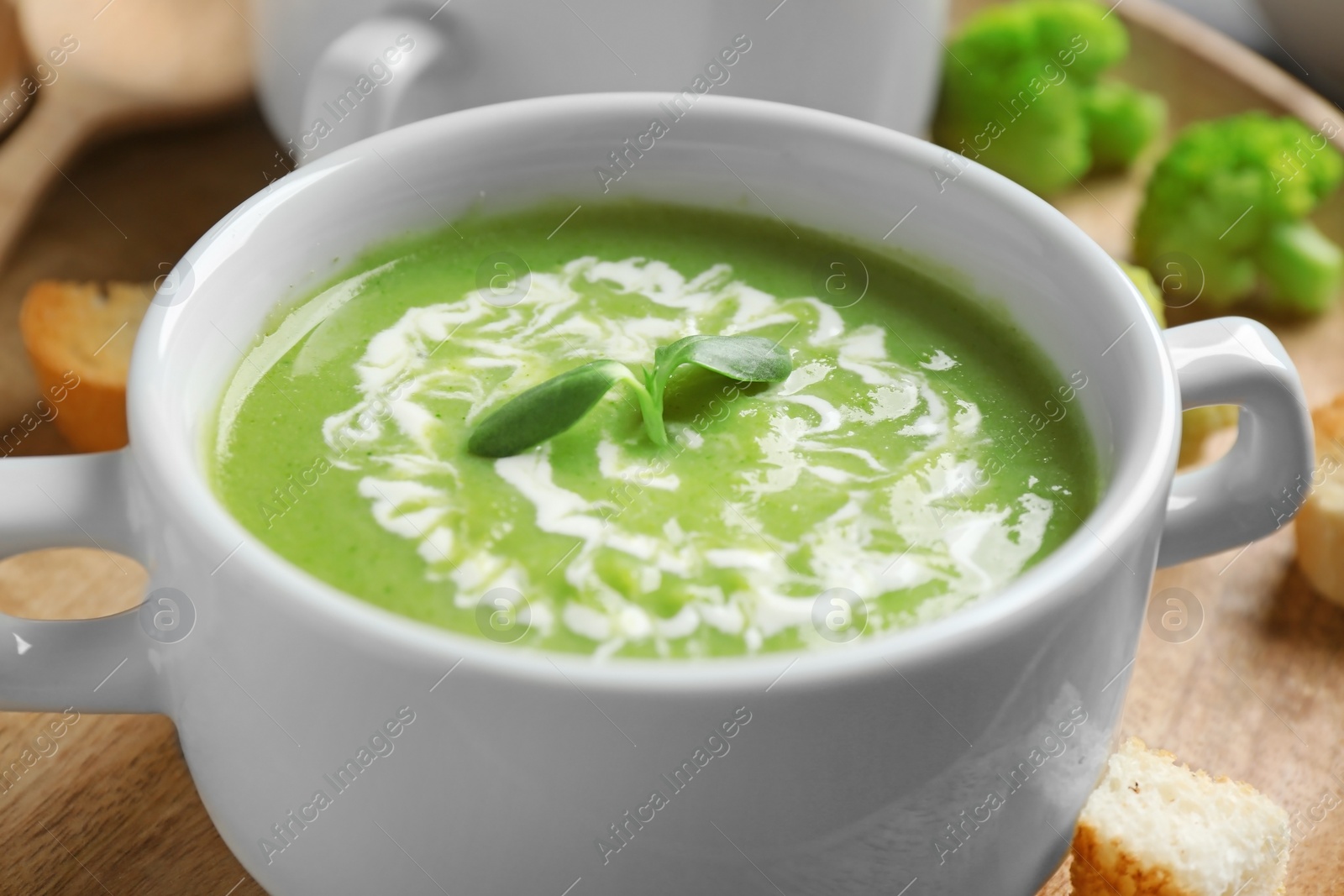 Photo of Bowl of delicious broccoli cream soup with microgreens served on tray, closeup