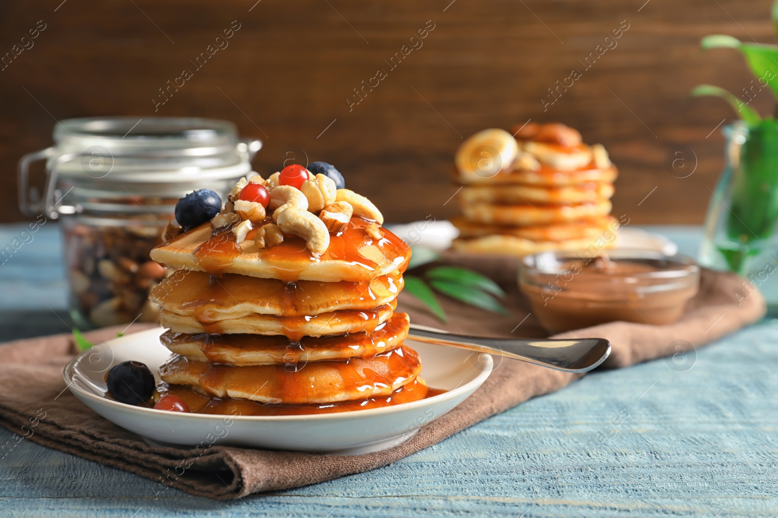 Photo of Stack of tasty pancakes with berries, nuts and syrup on table